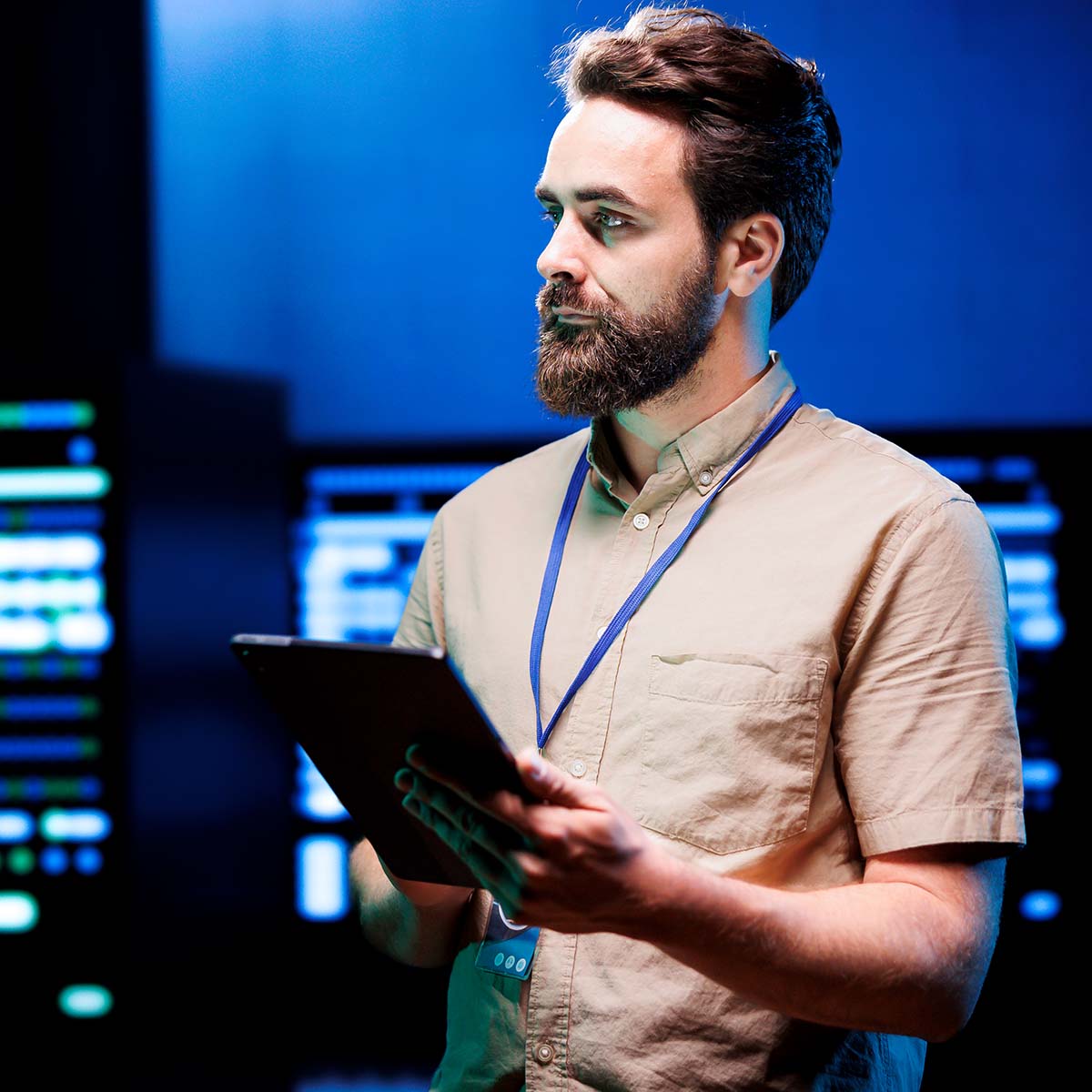 Das Bild zeigt einen Mitarbeiter in der IT-Operations-Abteilung, der den Serverraum kontrolliert. Er hält ein Tablet in der Hand, um die Serverstatus und -leistungen zu überwachen oder zu analysieren. Die Szene vermittelt eine professionelle und technische Arbeitsumgebung, in der der Mitarbeiter für die Aufrechterhaltung der Netzwerksicherheit und -stabilität verantwortlich ist.