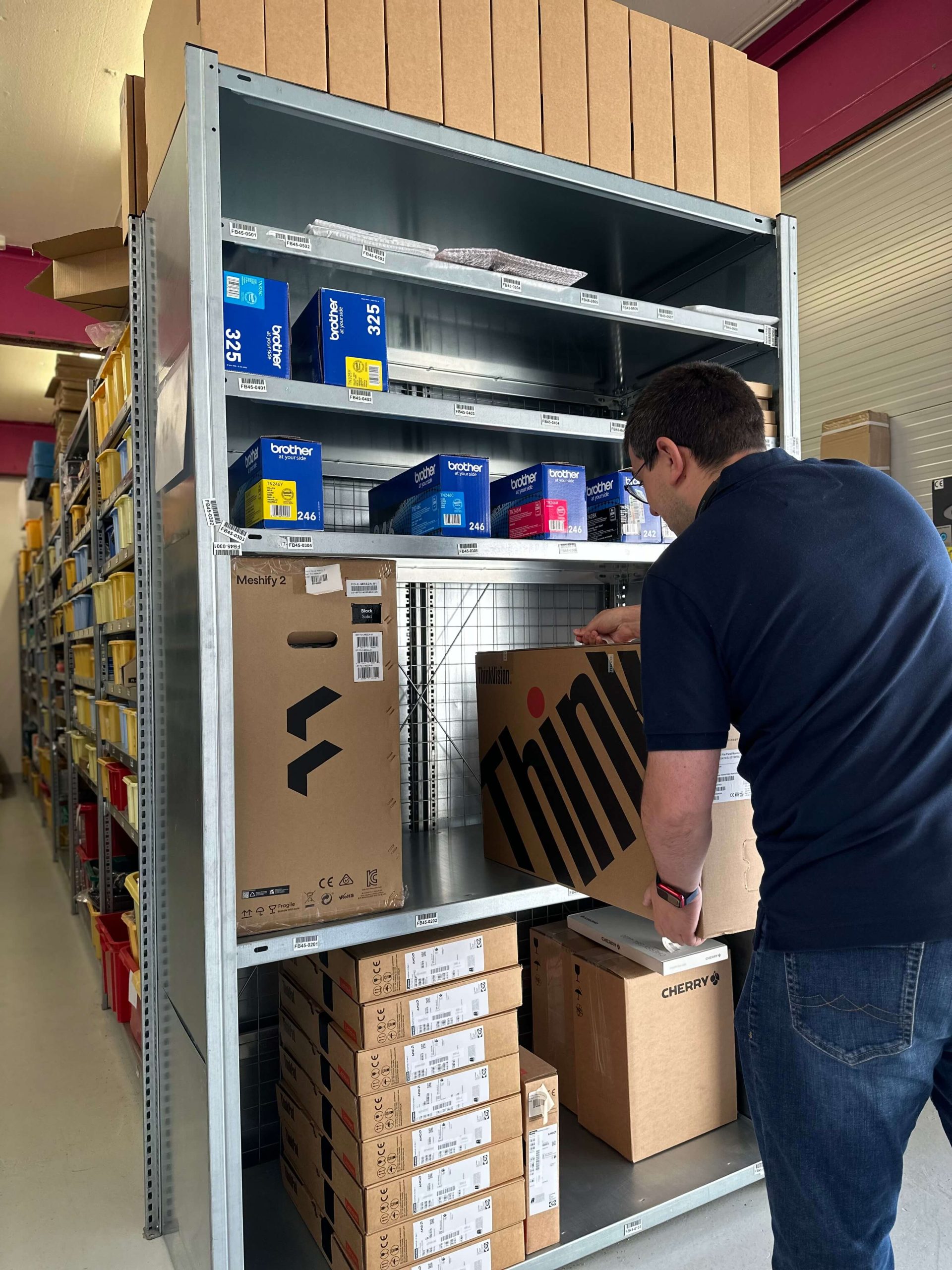 Das Bild zeigt einen Mitarbeiter, der einen ThinkPad-Karton im Regal verstaut. Die Szene vermittelt einen Einblick in den Arbeitsalltag im Lager und zeigt die sorgfältige Organisation der Produkte.